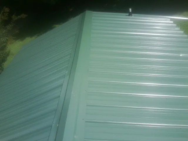 New green metal panels meeting at the ridge of a roof — Flat Roof Repair work by our crew in Rutland